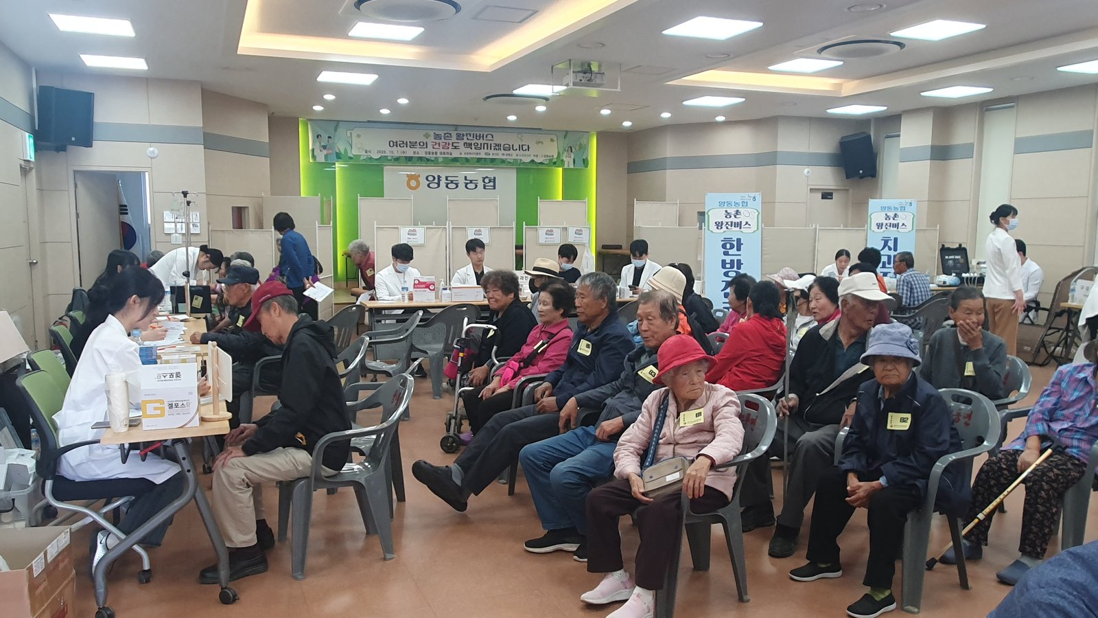 양동농협 대회의실에서 의자에 앉아 진료 순서를 기다리는 어르신들과 책상 앞에서 접수를 돕는 직원들의 모습